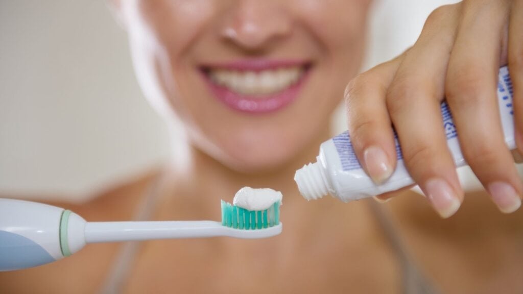 Person applying toothpaste to a toothbrush for oral hygiene.