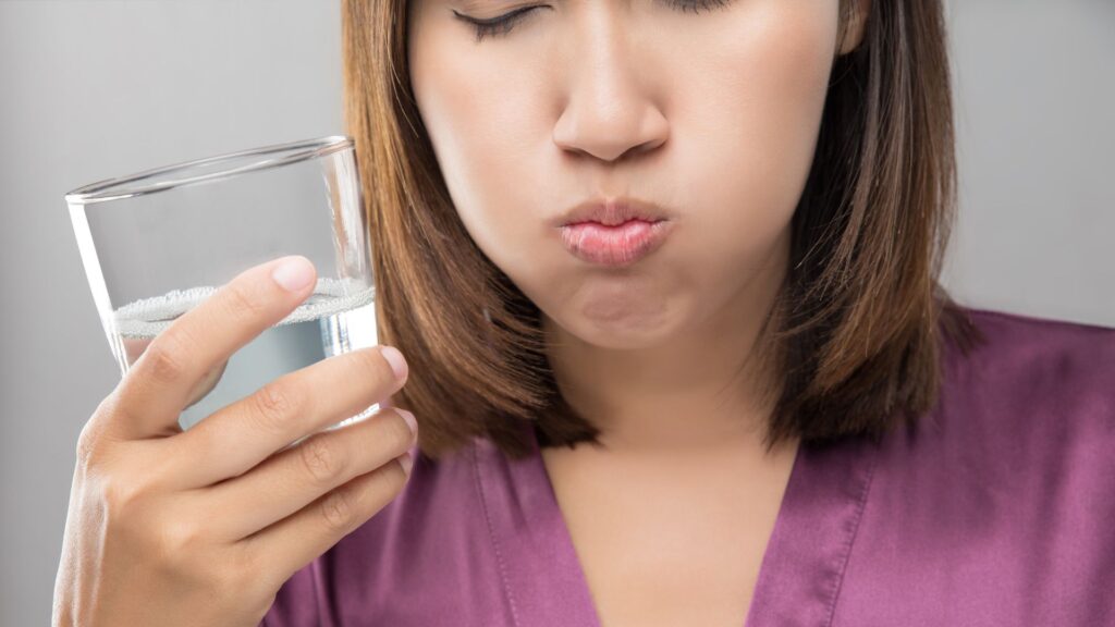 Woman holding a glass of water with a pained expression on her face.